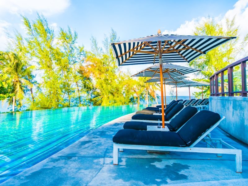 Beautiful luxury outdoor swimming pool in hotel resort with umbrella and chair on blue sky neary sea and ocean - Holiday vacation concept for background